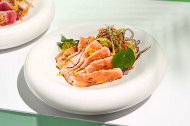 Susamlı somon balığı ve salata. Balık sashimi restoran aperatifi yeşil duvarlı beyaz masada. Tropik palmiye yapraklarının sert gölgesiyle gün ışığı. Yaz ya da bahar yemekleri