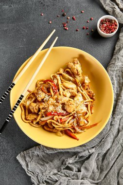 Tavuklu udon eriştesi. Tahta çubuklu sarı tabak. Koyu renk tahta masa. Asyalı, otantik gıda konsepti.