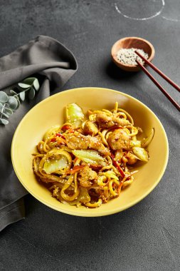 Körili Udon Eriştesi. Sarı tabakta Asya körili udon. Koyu tahtada ahşap yemek çubuğu. Asyalı, otantik gıda konsepti.