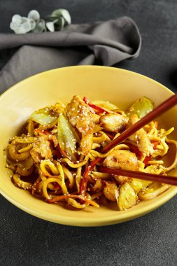 Körili Udon Eriştesi. Sarı tabakta Asya körili udon. Koyu tahtada ahşap yemek çubuğu. Asyalı, otantik gıda konsepti.