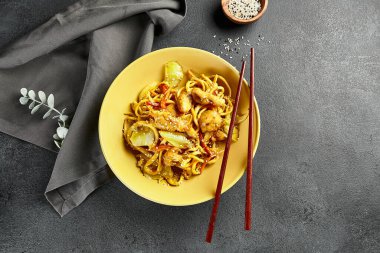 Körili Udon Eriştesi. Sarı tabakta Asya körili udon. Koyu tahtada ahşap yemek çubuğu. Asyalı, otantik gıda konsepti.