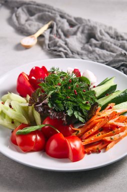 Çiğ yiyecek, taze sebze tabağı. Gri masada sağlıklı organik yiyecekler olan beyaz tabak. Domates, Kereviz, Salatalık ve Turp Sebze ve Taze Yeşiller. Üretim, Sağlıklı, Vejetaryen Kırsal Yemek Konsepti