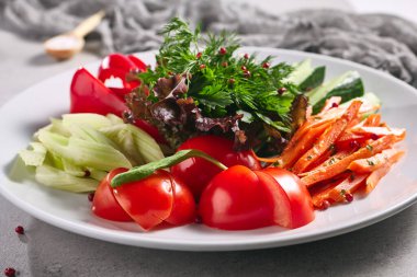 Çiğ yiyecek, taze sebze tabağı. Gri masada sağlıklı organik yiyecekler olan beyaz tabak. Domates, Kereviz, Salatalık ve Turp Sebze ve Taze Yeşiller. Üretim, Sağlıklı, Vejetaryen Kırsal Yemek Konsepti