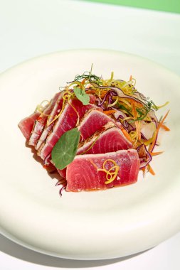 Susamlı ton balığı ve salata. Balık sashimi restoran aperatifi yeşil duvarlı beyaz masada. Tropik palmiye yapraklarının sert gölgesiyle gün ışığı. Yaz ya da bahar yemekleri
