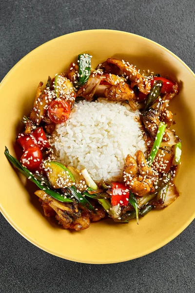 Sweet and Sour Chicken and Vegetables with Rice. Stir Fry Chicken with Vegetables and Sesame. Yellow plate with wooden chopstick on dark slate table. Chinese, asian, authentic food concept.