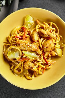 Körili Udon Eriştesi. Sarı tabakta Asya körili udon. Koyu tahtada ahşap yemek çubuğu. Asyalı, otantik gıda konsepti.