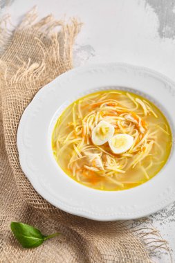 Bıldırcın yumurtalı tavuk çorbası. Beyaz kâse içinde ev usulü tavuk çorbası. Kırsal beyaz masa üzerinde, çuval peçeteli.