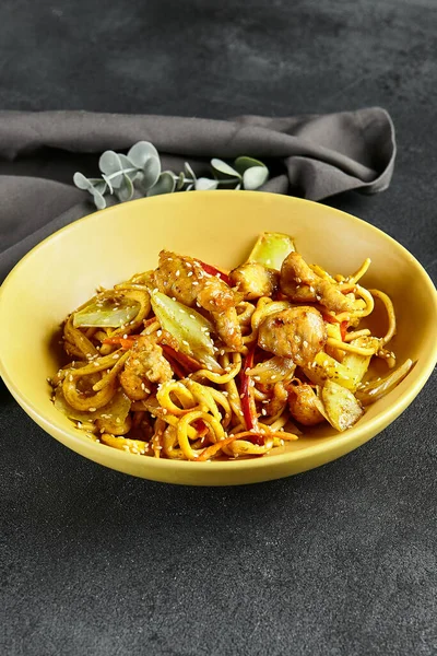 Körili Udon Eriştesi. Sarı tabakta Asya körili udon. Koyu tahtada ahşap yemek çubuğu. Asyalı, otantik gıda konsepti.