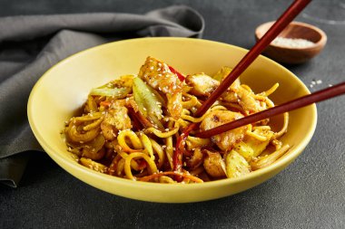 Körili Udon Eriştesi. Sarı tabakta Asya körili udon. Koyu tahtada ahşap yemek çubuğu. Asyalı, otantik gıda konsepti.