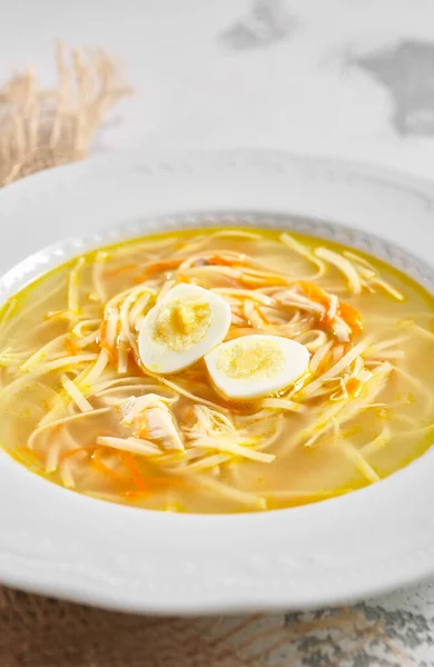 Chicken noodle soup with quail egg. Homestyle chicken noodle soup in white bowl on rustic white table with sack napkin