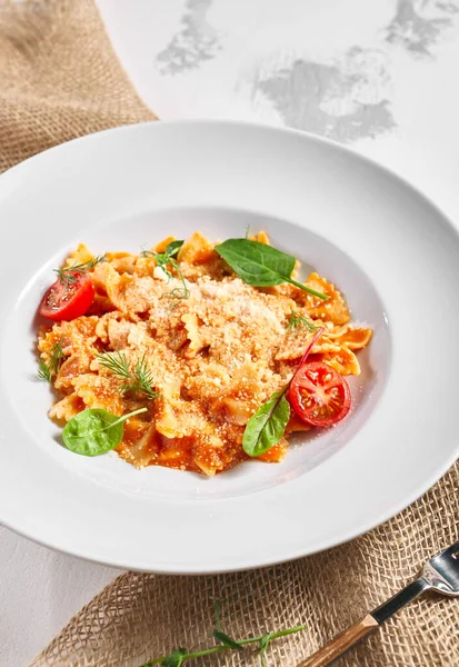 Farfalle pasta food on white table. Pasta restaurant plate with basil leaf and tomato, red tomato sauce. Delicious italian pasta