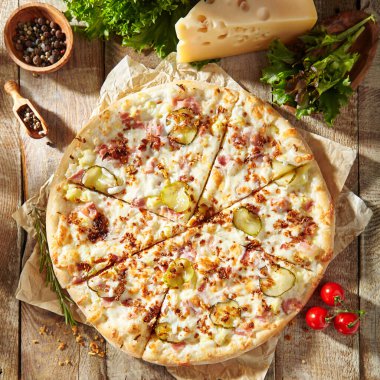 Jambonlu lezzetli pizza, turşu, kızarmış soğan ve salatalık turşusu. Parşömene süslenmiş ve ahşap masada pizza malzemeleri var. Kırsal stil, güneş ışığı