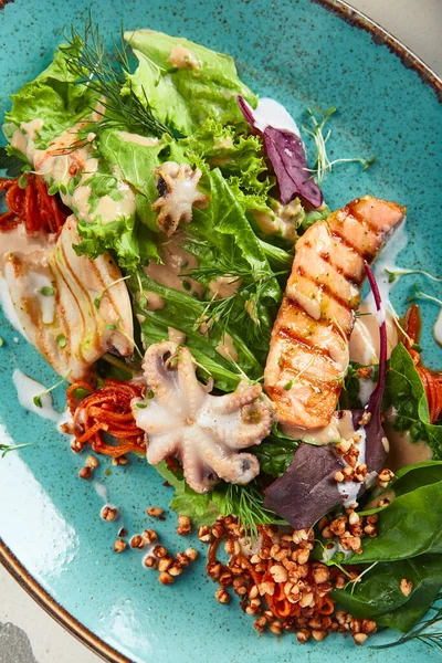 Çıtır karabuğday ve karışık sebzeli deniz ürünleri salatası. Karışık deniz mahsullü Frutti di Mare salatası - somon, kalamar, ahtapot. Mavi tabakta gurme restoran salatası.