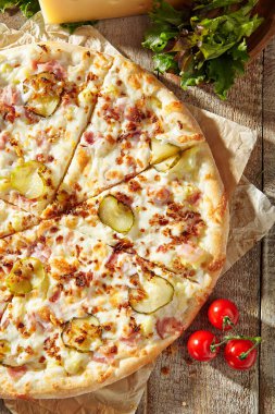 Jambonlu lezzetli pizza, turşu, kızarmış soğan ve salatalık turşusu. Parşömene süslenmiş ve ahşap masada pizza malzemeleri var. Kırsal stil, güneş ışığı