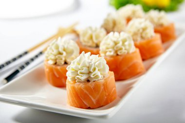 Füme somonla yapılmış Philadelphia Suşi Roll. Krem peynirli Maki suşisi. Beyaz masada tahta çubuklu beyaz tabak.