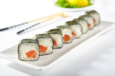 Füme somonla yapılmış Philadelphia Suşi Roll. Dışarıda deniz yosunu ve somon balığı ve krem peynirli Maki suşisi. Beyaz masada beyaz çubuklu beyaz tabak.