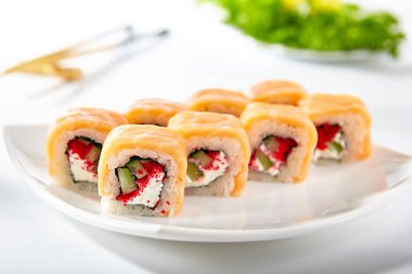 Somon Suşi Roll dışarıda füme somon ile yapılır. İçinde tobiko, salatalık ve krem peynirli Maki sake suşisi. Maki beyaz tabakta yuvarlanıyor ve beyaz masada ahşap çubuklar var.