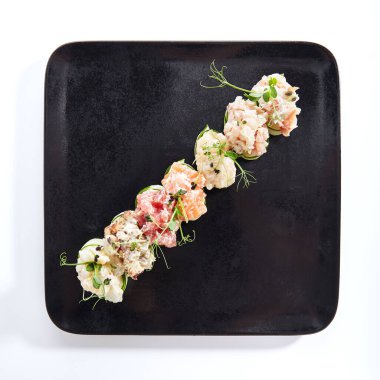 Salatalık ambalajlı suşi - Gunkan Maki suşisi, deniz ürünleri ve dilimlenmiş salatalık. Siyah tabakta lezzetli Gunkan suşisi. Beyaz arka planda izole edilmiş. Üst görünüm