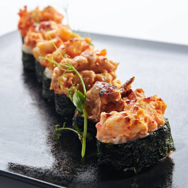 Gunkan Suşi, Gunkan Maki Suşi, deniz ürünleri ve baharatlı sos. İçinde pirinç olan suşi ve etrafına Norveç yosunu sarılmış. Siyah tabakta lezzetli Gunkan suşisi. Beyaz arkaplanda izole