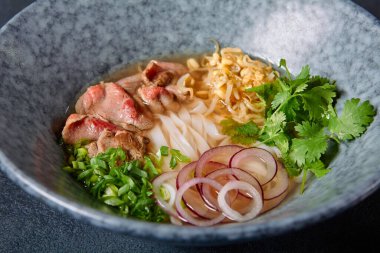 Vietnam mutfağı - Biftek Pho Erişte Çorbası veya Pho Bo Çorbası. Dokulu Koyu Gri Masa 'da Mavi Kasede Taze Yeşiller ile servis edildi. Baharatlı Pho Bo Çorbası