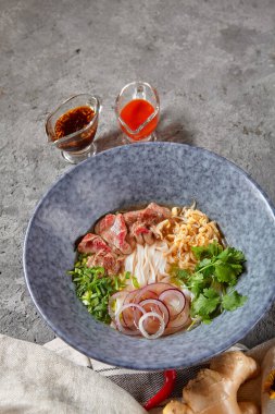 Vietnam mutfağı - Biftek Pho Erişte Çorbası veya Pho Bo Çorbası. Dokulu Koyu Gri Masa 'da Mavi Kasede Taze Yeşiller ile servis edildi. Baharatlı Pho Bo Çorbası