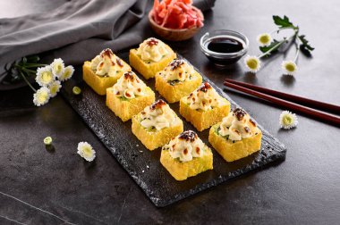 Uluslararası tempura suşisi siyah tabakta yuvarlanıyor. Krem peynirli kızarmış suşi rulosu. Ahşap çubuk, soya sosu ve turşulu zencefille servis edilir. Tempura maki suşili Japon seti.