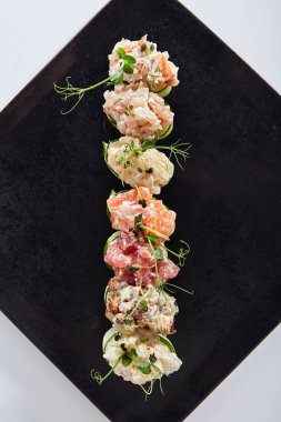 Salatalık ambalajlı suşi - Gunkan Maki suşisi, deniz ürünleri ve dilimlenmiş salatalık. Siyah tabakta lezzetli Gunkan suşisi. Beyaz arka planda izole edilmiş. Üst görünüm