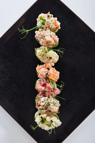 Salatalık ambalajlı suşi - Gunkan Maki suşisi, deniz ürünleri ve dilimlenmiş salatalık. Siyah tabakta lezzetli Gunkan suşisi. Beyaz arka planda izole edilmiş. Üst görünüm