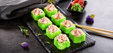 Uluslararası maki suşisi siyah tabakta yuvarlanıyor. Tahta çubuk, yeşil wasabi ve turşulu zencefil ile servis edilir. Japon seti, koyu taştan arka planda maki suşi rulosu..