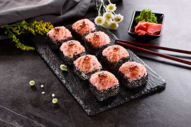 Uluslararası maki suşisi siyah tabakta yuvarlanıyor. Tahta çubuk, yeşil wasabi ve turşulu zencefil ile servis edilir. Japon seti, koyu taştan arka planda maki suşi rulosu..