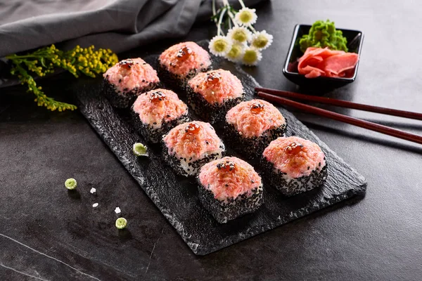 Uluslararası maki suşisi siyah tabakta yuvarlanıyor. Tahta çubuk, yeşil wasabi ve turşulu zencefil ile servis edilir. Japon seti, koyu taştan arka planda maki suşi rulosu..