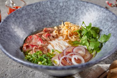 Vietnam mutfağı - Biftek Pho Erişte Çorbası veya Pho Bo Çorbası. Dokulu Koyu Gri Masa 'da Mavi Kasede Taze Yeşiller ile servis edildi. Baharatlı Pho Bo Çorbası