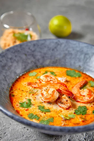 Tom Yum or Tom Yam Soup - Hot and Sour Thai Soup cooked with Shrimp. Thai Authentic Traditional Dinner. Soup in Blue Bowl on Dark Grey Table. Street Asian Food