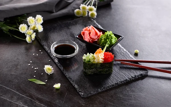 Seaweed wrapped sushi - Gunkan Maki Sushi with Seafood and Tobiko Caviar. Delicious Gunkan Sushi on black slate plate with soy sauce dip. Black stone background