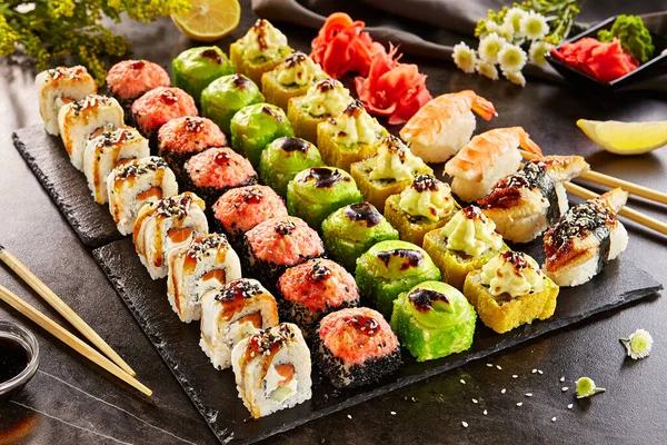 Sushi bar set - International maki sushi roll on black slate platter. Served with wooden chopstick, wasabi and pickled ginger. Japanese set with maki sushi roll and nigiri sushi on dark stone table