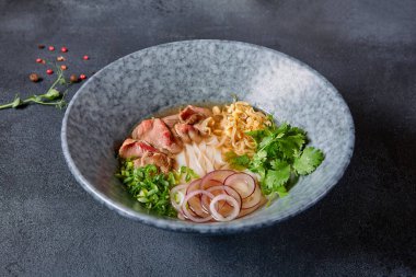 Vietnam mutfağı - Biftek Pho Erişte Çorbası veya Pho Bo Çorbası. Dokulu Koyu Gri Masa 'da Mavi Kasede Taze Yeşiller ile servis edildi. Baharatlı Pho Bo Çorbası