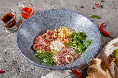 Vietnam mutfağı - Biftek Pho Erişte Çorbası veya Pho Bo Çorbası. Dokulu Koyu Gri Masa 'da Mavi Kasede Taze Yeşiller ile servis edildi. Baharatlı Pho Bo Çorbası