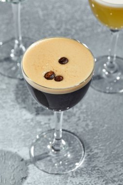 Kahve Ekşi Kokteyl, köpüklü kahve bazlı likör kokteyli. Güneş ışığı ve gölgesi olan eski bir masa. Üzerine kahve tohumu dökülmüş sert bir içki.