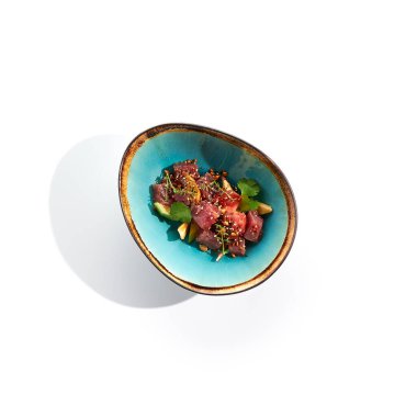 Ton balığı ve avokado salatası kasesi. Mavi salata kasesi beyaz arka planda izole edilmiş. Mikro yeşillik ve susam ile süslenmiş salata, doğranmış ton balığı, dilimlenmiş avokado ve maydanoz yeşil yaprak. Baharatlı soslu çiğ ton balığı.