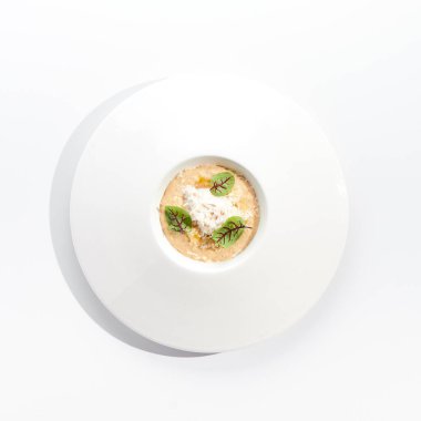 Beyaz restoran tabağında yengeç etli risotto. Parmesan peyniri ve yeşil yapraklarla süslenmiş. Beyaz arka planda izole edilmiş beyaz soslu lezzetli yengeç etli risotto. Deniz mahsullü pilav