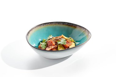 Somon ve avokado salatası kasesi. Mavi salata kasesi beyaz arka planda izole edilmiş. Mikro yeşillik ve susam ile süslenmiş salata, doğranmış somon, dilimlenmiş avokado ve maydanoz yeşil yaprak. Baharat soslu çiğ somon