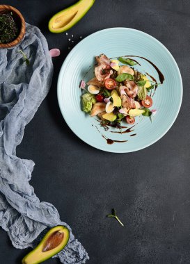 Avokadolu salata, hindi eti ve pastırma. Koyu dokulu masada mavi tabak. Restoran, keto diyet danışmanı.
