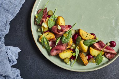 Biftekli salata ve fırında patates. Taze ıspanakla süslenmiş. Siyah desenli masada yeşil tabak. Restoran, gurme yemek konsepti.