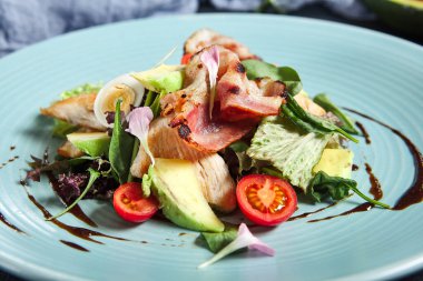 Avokadolu salata, hindi eti ve pastırma. Koyu dokulu masada mavi tabak. Restoran, keto diyet danışmanı.