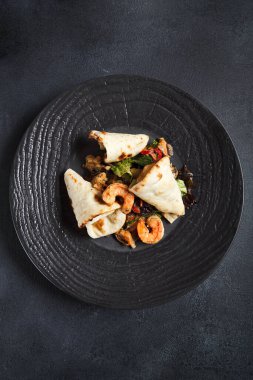 Karides ve pita ekmekli salata. Siyah seramik tabakta deniz ürünleri ve sebzeler. Gurme, restoran sağlıklı gıda konsepti. Koyu dokulu masa