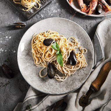 Deniz ürünleri ve yeşil yapraklı ev yapımı makarna. Gri antika masa ve kumaş. Midyeli makarna.