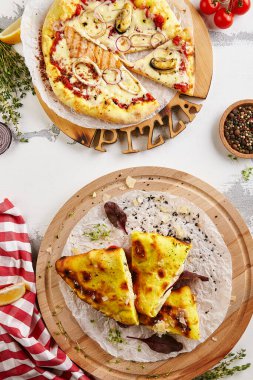 Deniz mahsulleri pizzası ve calzone üst görünümü. Karışık deniz ürünleri, somon, midye ve kalamar. Fesleğen yapraklı tavuk calzone pizza. İçindekiler ve pizza tahtası beyaz masa görünümünde.