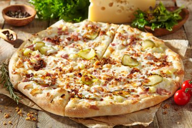 Jambonlu lezzetli pizza, turşu, kızarmış soğan ve salatalık turşusu. Parşömene süslenmiş ve ahşap masada pizza malzemeleri var. Kırsal stil, güneş ışığı