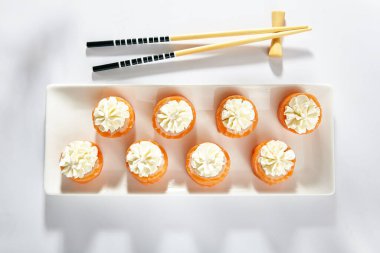 Füme somonla yapılmış Philadelphia Suşi Roll. Krem peynirli Maki suşisi. Beyaz masada tahta çubuklu beyaz tabak. Üst görünüm