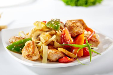 Tatlı ve ekşi tavuk ve sebzeli Udon eriştesi. Beyaz arka planda Asya usulü şehriye. Udon beyaz tabakta, ahşap çubuklarla